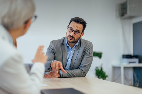 Two people in business attire are having a serious conversation about forecasting mistakes and solutions for them at a desk in a modern office setting.