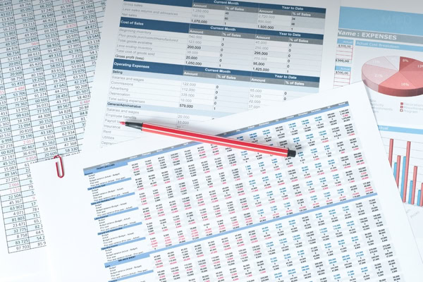 Several financial spreadsheets and charts with numerical data are spread out on a desk, with a red pen and a red paperclip placed on top of the papers, showcasing investor preparation and lender readiness. How to Prepare for Investors, Lenders, or a Sale