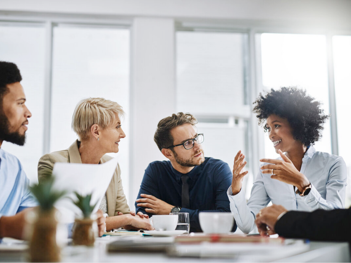 Four people sit at a table in a bright office, engaged in a discussion about whether hiring a fractional CFO is worth it, with documents, coffee cups, and a laptop in front of them.